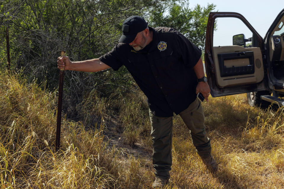 Jim Hogg County Sheriff's Investigator Ruben Garza investigates the location of a missing water station for immigrants containing sealed jugs of fresh water along a fence line near a roadway in rural Jim Hogg County, Texas, Tuesday, July 25, 2023. The South Texas Human Rights Center maintains over 100 blue barrels consistently stocked with water across rural South Texas to serve as a life-saving measure for immigrants who have crossed into the United States to travel north in the sweltering heat. (AP Photo/Michael Gonzalez)