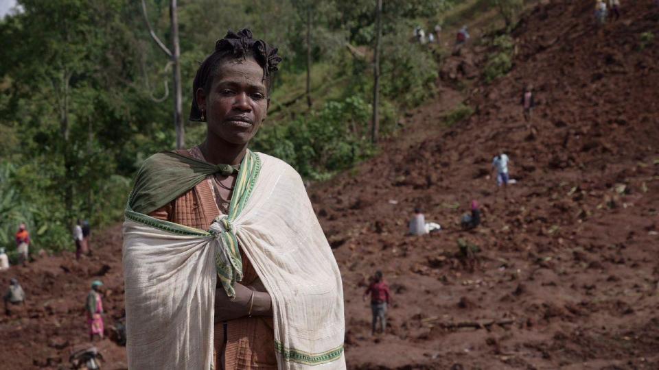 A woman looks at the camera while others in the background dig for survivors in Gofa zone, Ethiopia - Thursday 25 July 2024