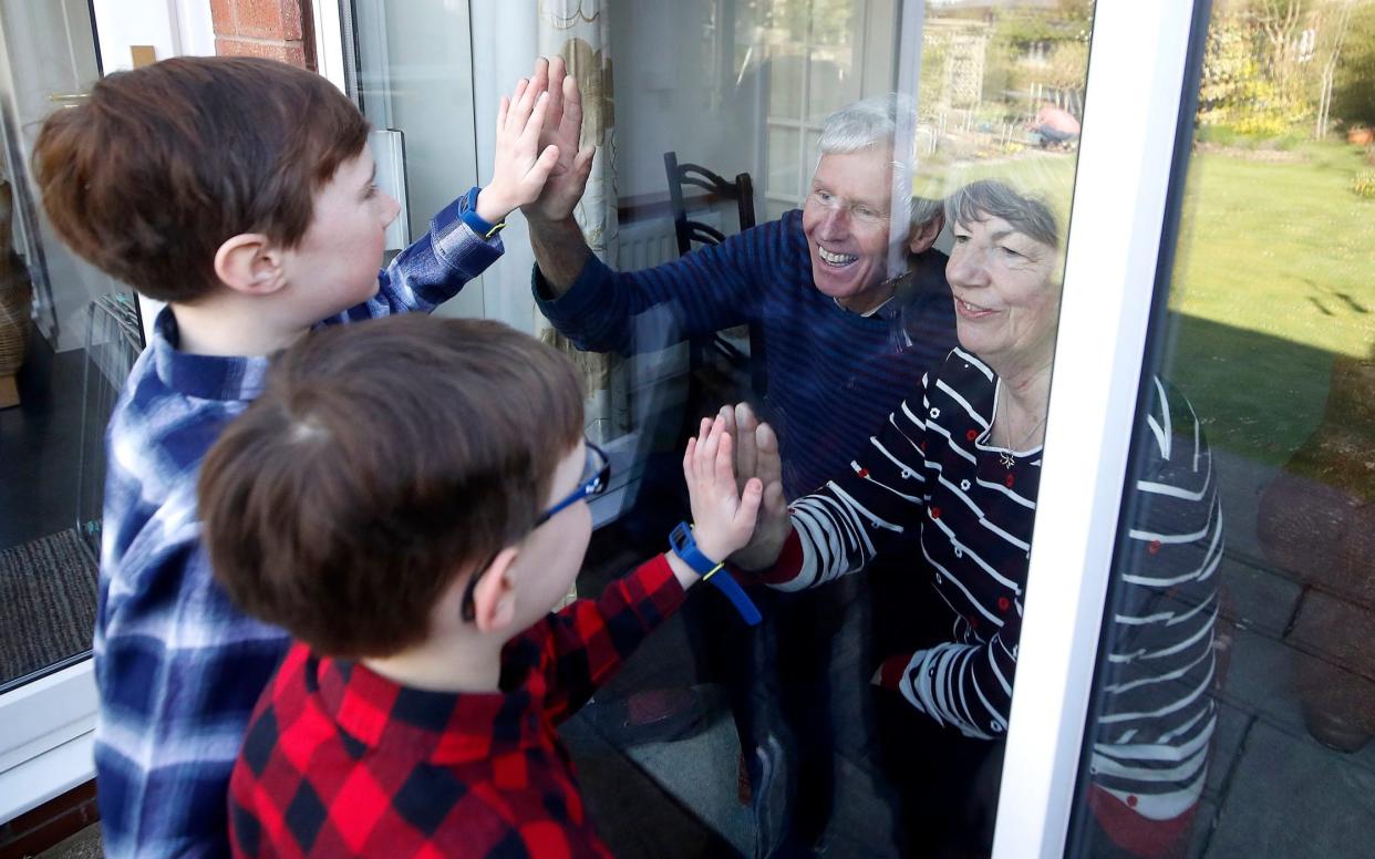 Ben and Isaac talk to their grandparents Sue and Alan through a window, as they self-isolate at their home in Knutsford, Cheshire - Martin Rickett/PA