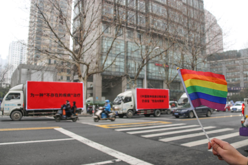 This photo taken on January 14, 2019 shows an activist (R) waving a rainbow flag near three trucks with slogans opposing "gay conversion therapy" in Nanjing. - A Chinese artist and a gay policeman have launched an unusually high-profile public protest campaign in which bright-red trucks bearing slogans denouncing homosexual "conversion therapy" are being driven through several major cities. (Photo by STR / AFP) / China OUT (Photo credit should read STR/AFP via Getty Images)