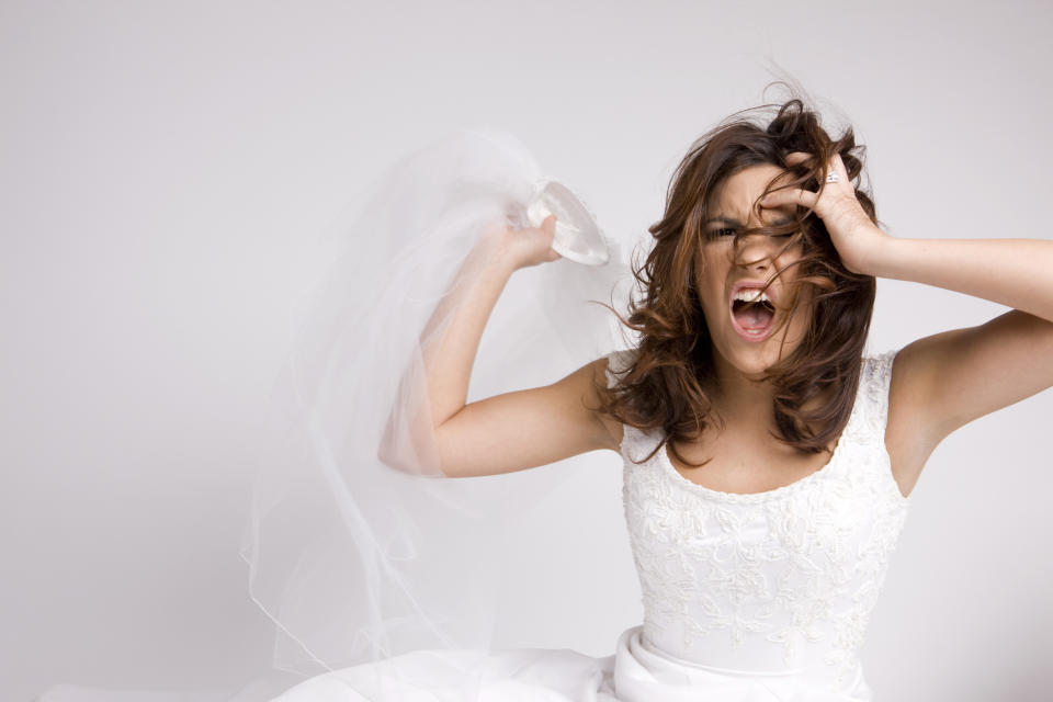 A woman in a wedding dress screams while pulling at her hair, holding a veil in one hand, expressing frustration