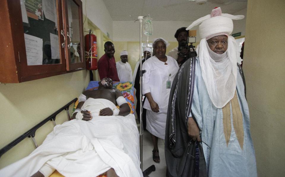 An unidentified local chief walk past a victim of Monday's explosion at Asokoro hospital in Abuja, Nigeria, Tuesday, April 15, 2014, with dozens feared dead as the blast destroyed more than 30 vehicles and caused secondary explosions as their fuel tanks exploded and burned. The Monday attack just miles from Nigeria's seat of government increases doubts about the military's ability to contain an Islamic uprising that is dividing the country on religious lines as never before.(AP Photo/ Sunday Alamba)