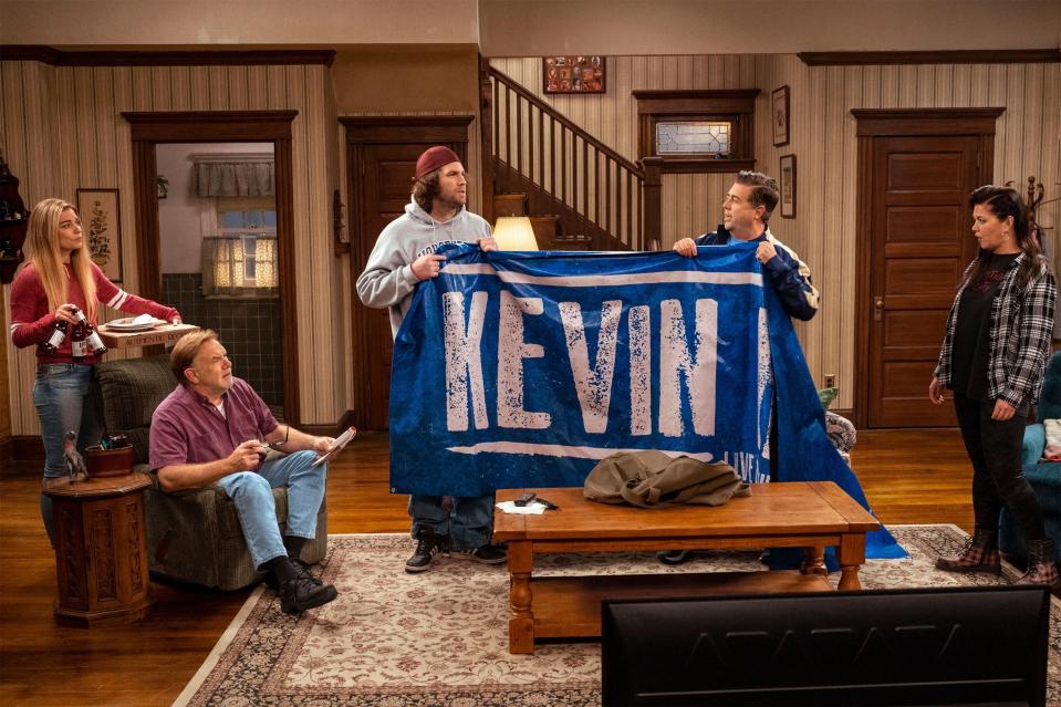 in the sitcom living room, kevin's friends hold up a giant blanket reading "Kevin"