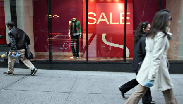 Pedestrians walk in front of large sale signs in the front w
