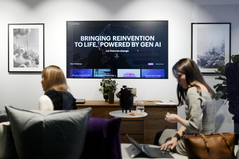 People sitting in a lounge inside a building at the Davos Promenade with a screen displaying a slogan about AI, alongside the World Economic Forum in Davos, Switzerland, Thursday, Jan. 18, 2024. The AI technology has taken a large and growing slice of attention in Davos, this year the theme of Artificial Intelligence "as a driving force for the economy and society" will get about 30 separate sessions. (AP Photo/Markus Schreiber)