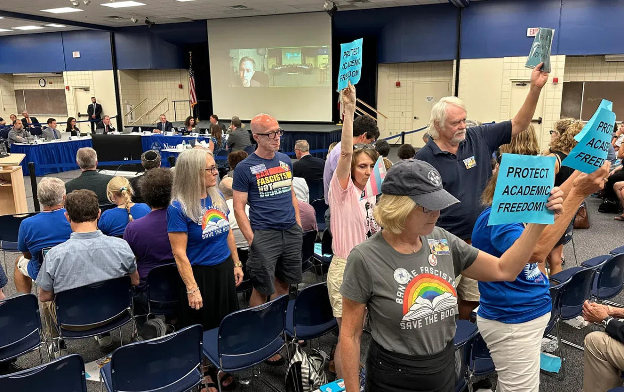Members of the audience turn their backs and hold up "Protect Academic Freedom" signs after the board of trustees of New College denies early tenure to five professors at a meeting in April 2023. Some protesters are wearing T-shirts with the words, "BAN THE FASCISTS SAVE THE BOOKS."