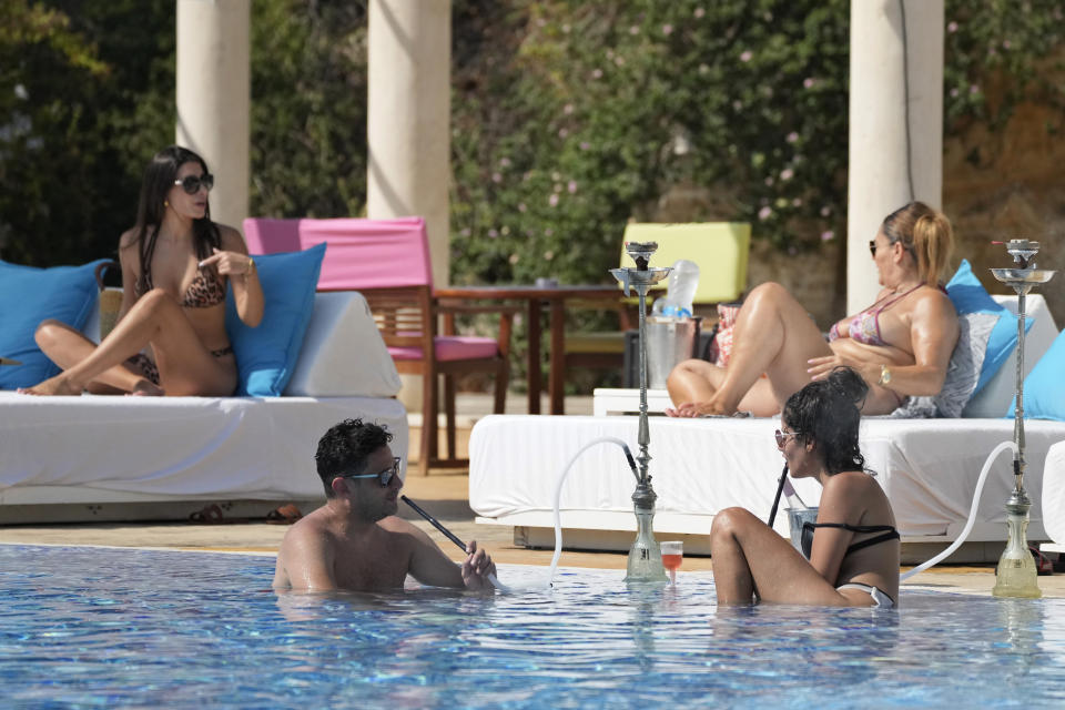 A couple smoke a traditional "shisha" water pipe as they sit in a swimming pool at the Edde Sands beach resort in the ancient Phoenician city of Byblos north of Beirut, Lebanon, Friday, July 2, 2021. With their dollars trapped in the bank, a lack of functioning credit cards and travel restrictions imposed because of the pandemic, many Lebanese who traditionally vacationed over the summer at regional hotspots are also now turning toward domestic tourism. (AP Photo/Hassan Ammar)