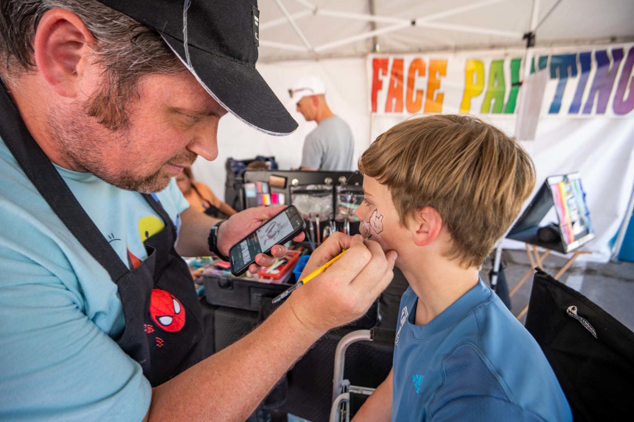 Lawrence Grech of LOL Cartoons paints a youngster's face in the children's area at the Downtown Edmond Arts Festival.