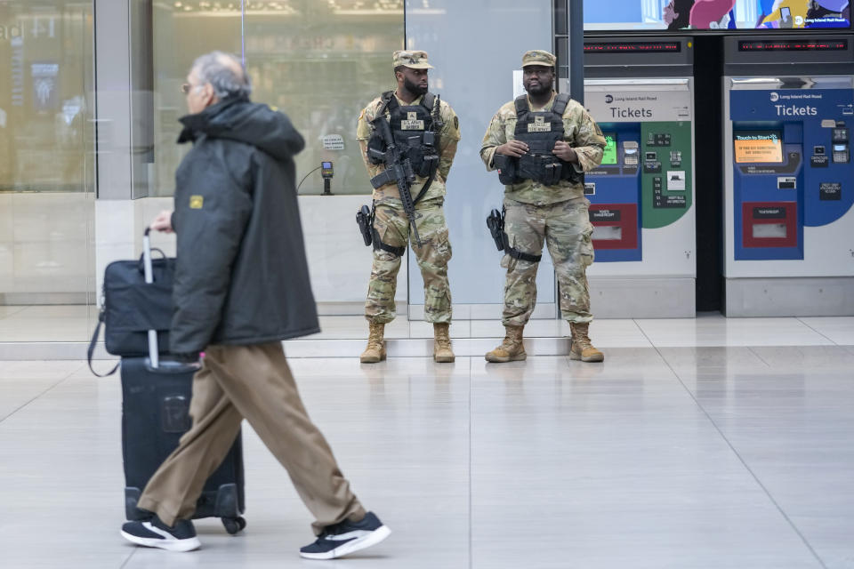 A commuter walks past a couple of New York National Guards soldiers stand guard a the Moynihan Train Hall at Penn Station, Thursday, March 7, 2024, in New York. New York Gov. Kathy Hochul announced plans Wednesday to send the National Guard to the New York City subway system to help police conduct random searches of riders' bags for weapons following a series of high-profile crimes on city trains. (AP Photo/Mary Altaffer)