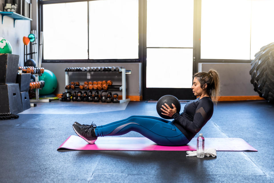 Stock photo of young attractive woman doing sit-ups with a medicine ball in a gym.