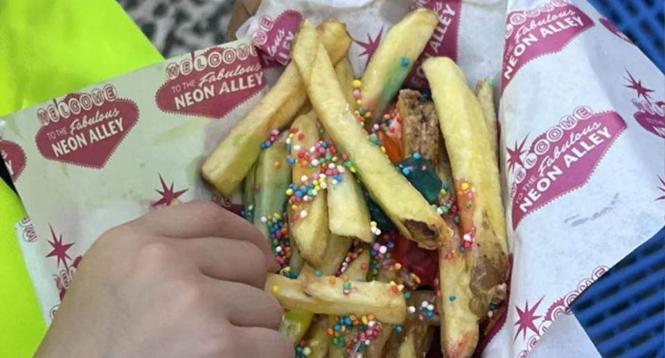 A basket with greaseproof paper is loaded with fries and gummy bears, with a hand pinching another chip at the Sydney Royal Easter Show. 