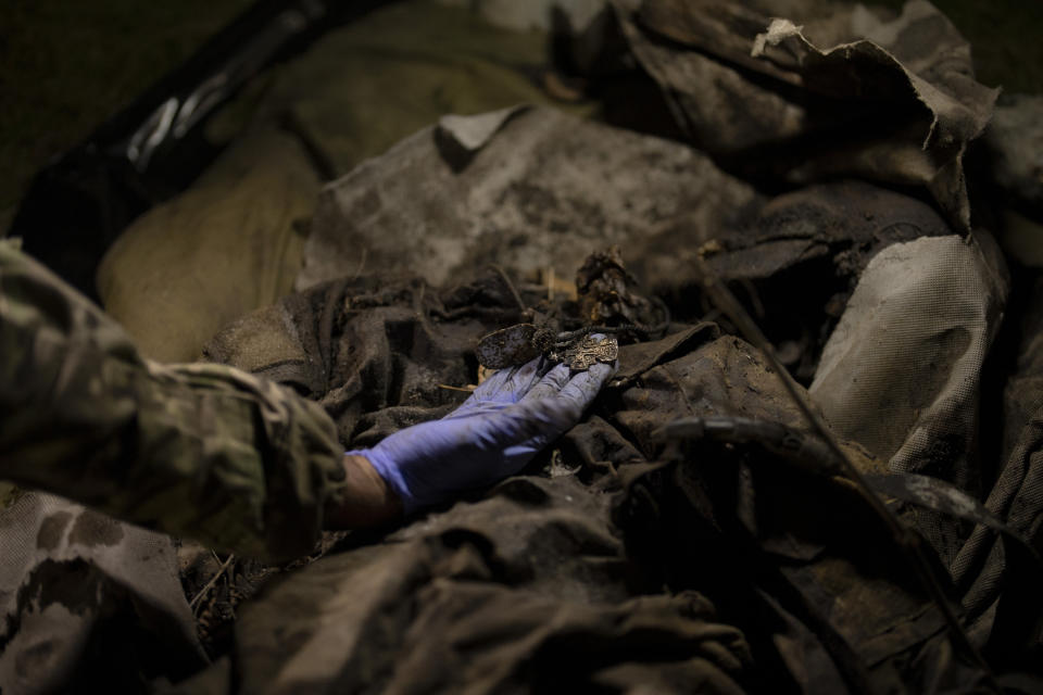 Oleksii Yukov inspects the necklace of a deceased Russian soldier in Sloviansk region, Ukraine, Tuesday, Oct. 24, 2023. “We are not fighting the dead,” he said. “I don’t separate the bodies of Russian soldiers and Ukrainian soldiers. They are all souls for me.” (AP Photo/Bram Janssen)