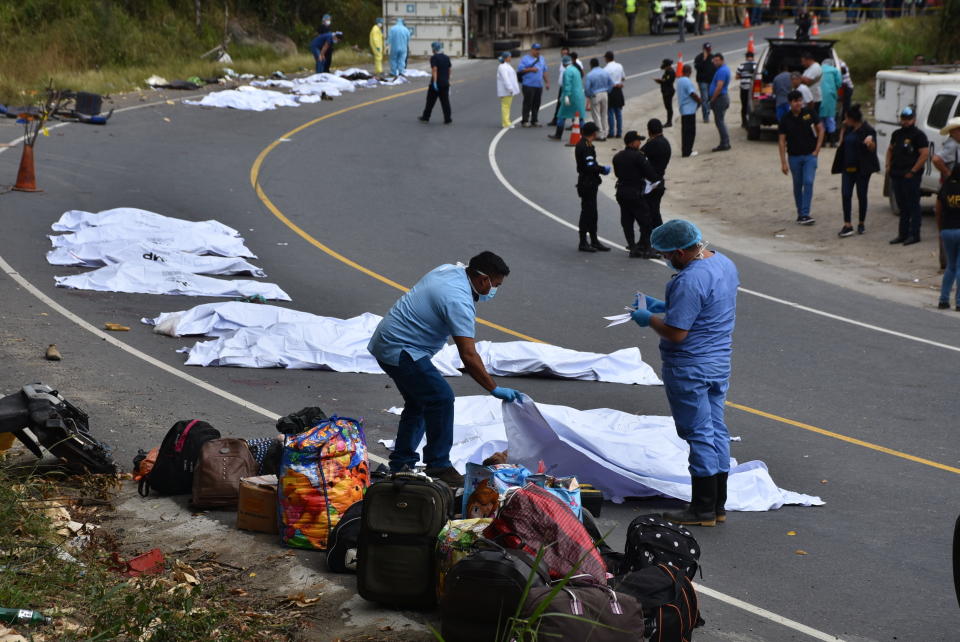 Forensic workers cover the bodies of passengers that perished in bus that crashed with a trailer truck in Gualan, Guatemala, Saturday, Dec. 21, 2019. The accident killed at least 21 people and left a dozen wounded, according to the national disaster agency. (AP Photo/Carlos Cruz)