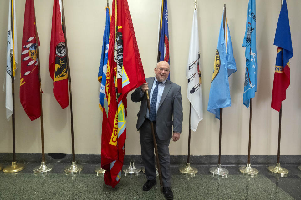 Tracy Toulou, the outgoing Director of the Office of Tribal Justice, holds the flag of the Colville Confederated Tribes, his tribal affiliation, alongside flags of tribal nations at the Department of Justice, Thursday, March 14, 2024, in Washington. For more than two decades, Toulou has confronted the serious public safety challenges facing Indian Country by working to expand the power of tribal justice systems. Today, tribal law enforcement finally has a seat at the table when federal authorities coordinate with state and local police, according to the Justice Department’s point person on Native American tribes. (AP Photo/Mark Schiefelbein)