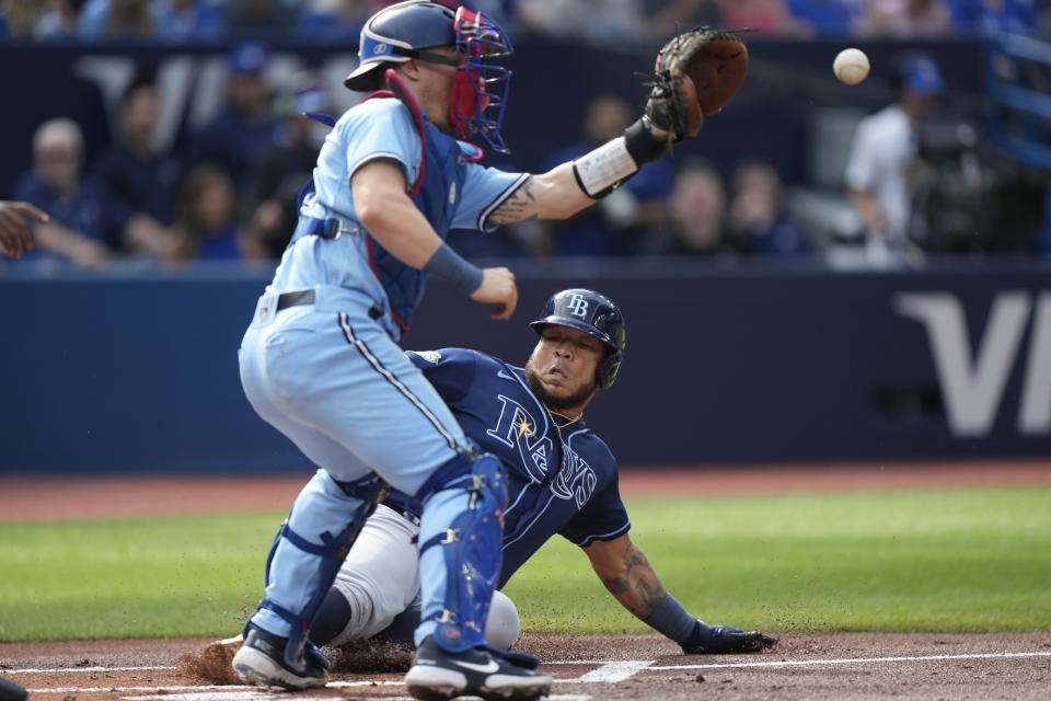 Tampa Bay Rays designated hitter Harold Ramirez, bottom, slides into home plate to score in front of Toronto Blue Jays catcher Tyler Heineman, top, during first-inning baseball game action in Toronto, Sunday, Oct. 1, 2023. (Frank Gunn/The Canadian Press via AP)