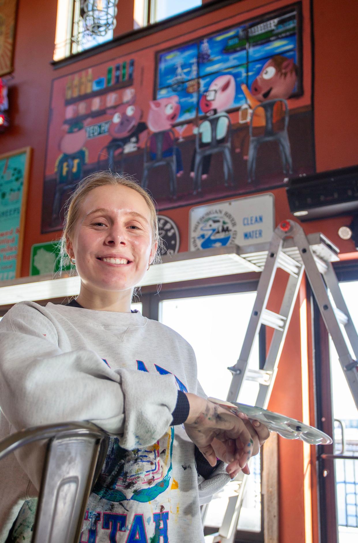 Mary Athorp, of Howards Grove, Wis., poses, Thursday, January 18, 2024, by the mural she created for Parker Johns at their Sheboygan, Wis., location,