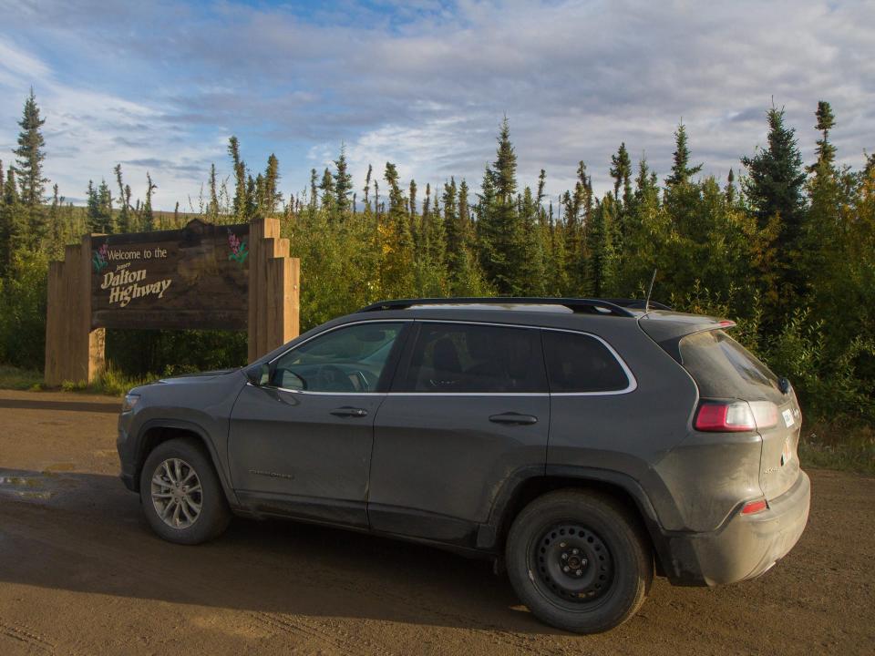 A car parked in front of the sign for the Dalton Highway in Alaska.