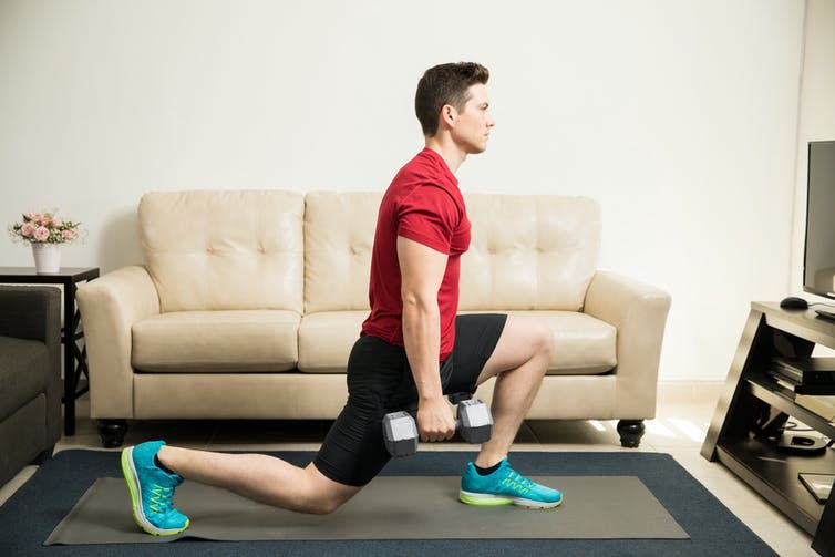 A young man performs a lunge with two dumbbells in his hands.