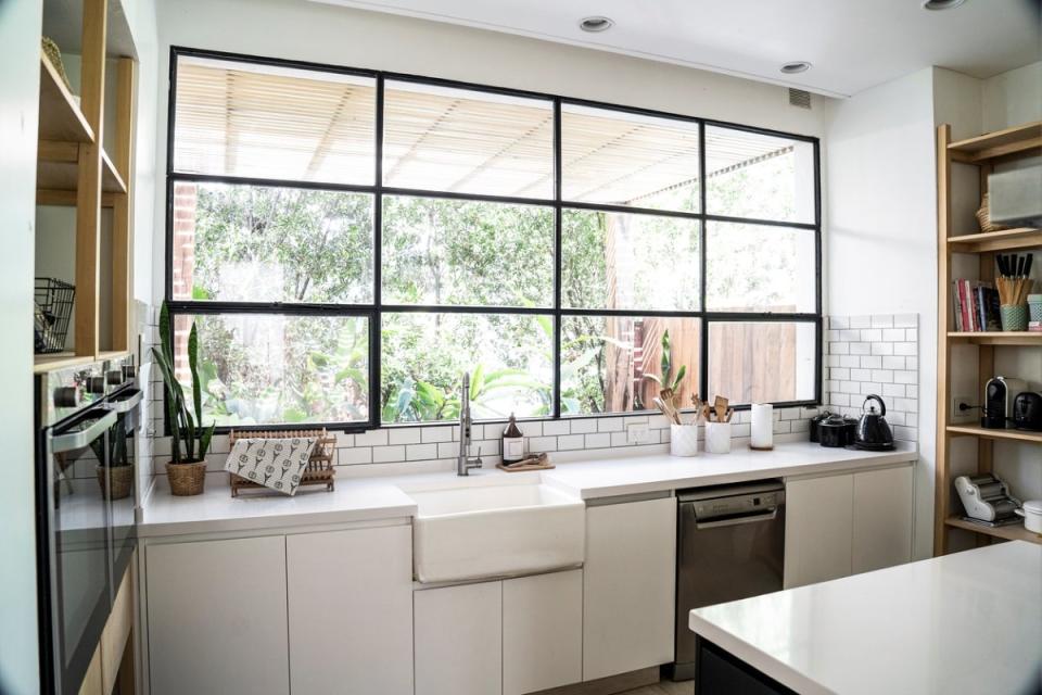 Kitchen grid window without curtains, with black metal window frames, in a mostly white, contemporary kitchen.