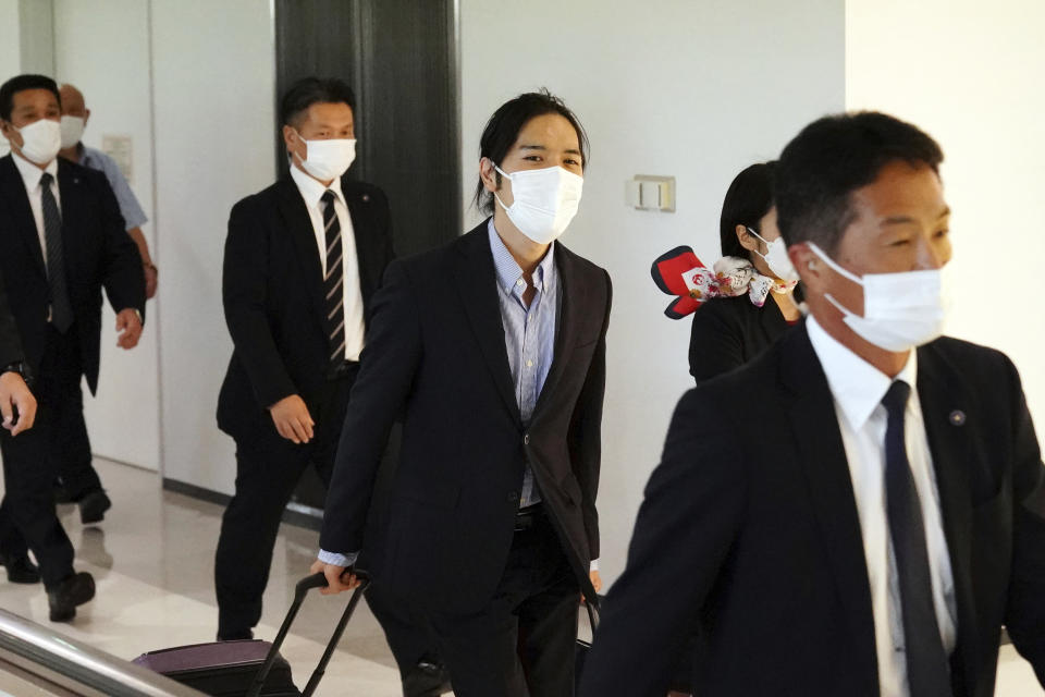 Kei Komuro, center, fiance of Japan's Princess Mako, is escorted by security personnel as he leaves the Narita International Airport in Narita, near Tokyo, Monday, Sept. 27, 2021, after returning to Japan from the United States. (AP Photo/Eugene Hoshiko)