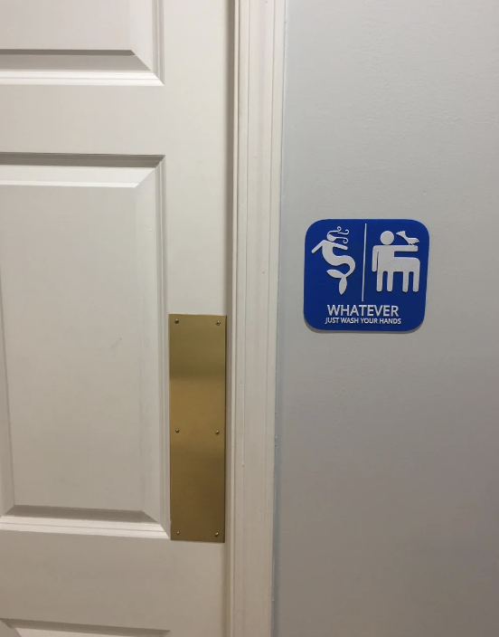 Door with humorous restroom sign featuring symbols for all genders, stating, "Whatever, just wash your hands."
