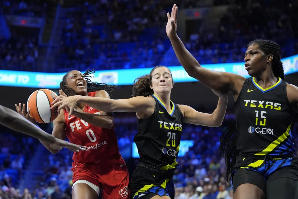 Indiana Fever guard Kelsey Mitchell (0) is fouled while shooting by Dallas Wings' Maddy Siegrist (20) as Wings center Teaira McCowan (15) helps defend in the first half of a WNBA basketball game Sunday, Sept. 1, 2024, in Arlington, Texas. (AP Photo/Tony Gutierrez)