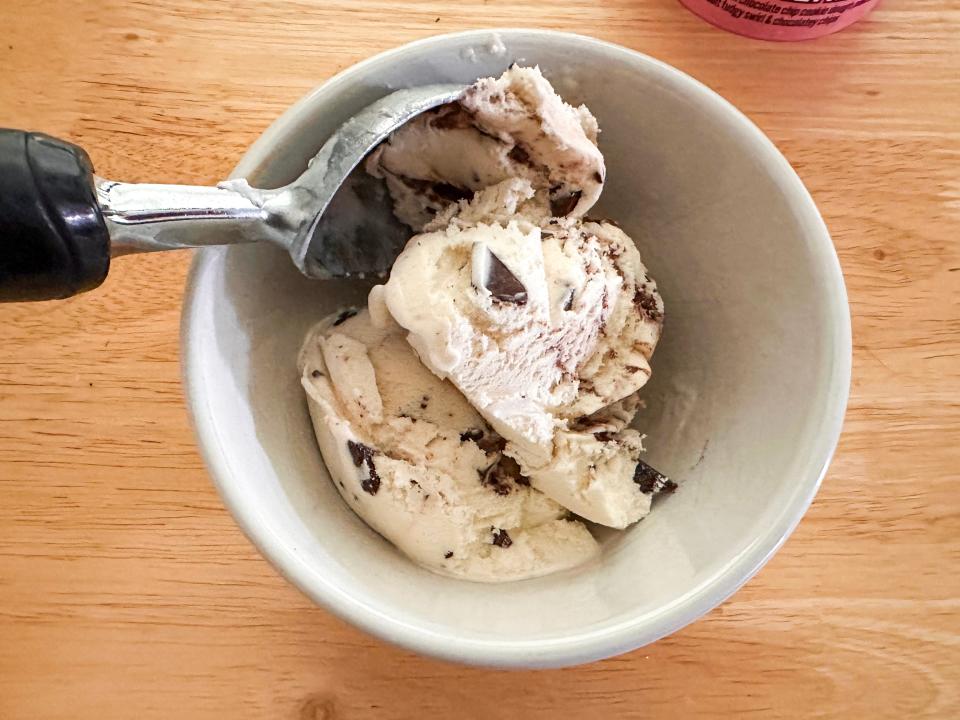 Bird's eye view of a white bowl of a white ice cream with chocolate chips and fudge. An ice cream scoop sticks out of the bowl