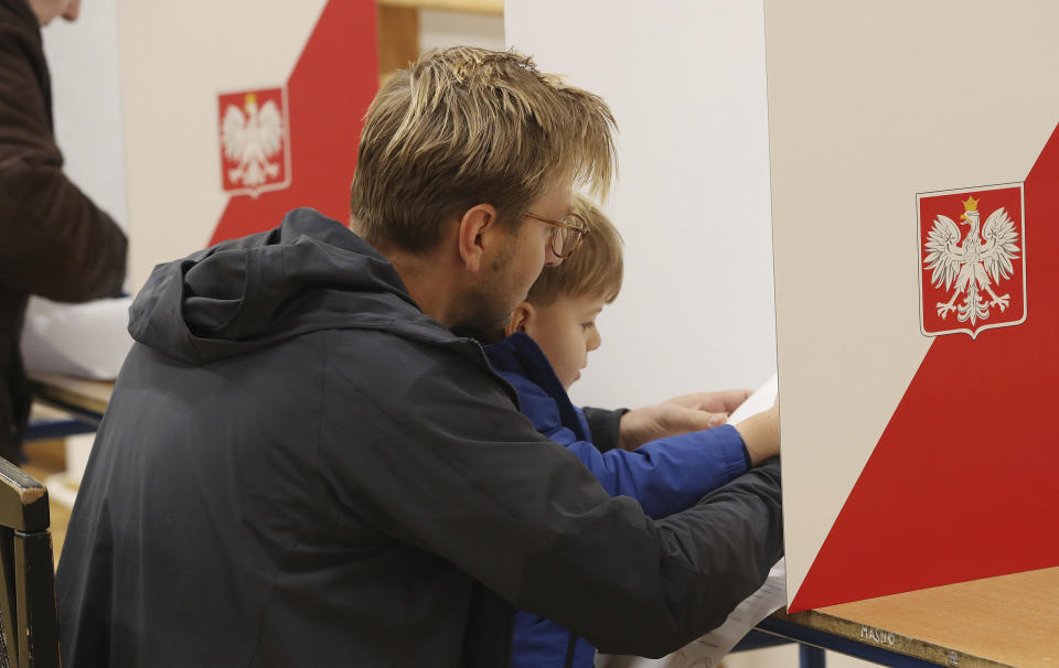 A man fills out his ballot with the help of his son in elections to the Polish parliament in Warsaw, Poland, on Oct. 13, 2019. Poles are voting Sunday in a parliamentary election, that the ruling party of Jaroslaw Kaczynski is favored to win easily, buoyed by the popularity of its social conservatism and generous social spending policies that have reduced poverty. Critics, however, fear that another term for the party, whose term has included an erosion of the rule of law, will mark a further decline in democracy. (AP Photo/Czarek Sokolowski)