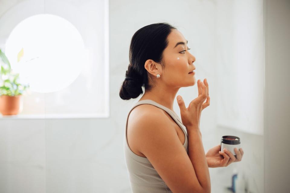 Morning Routine: Attractive Asian Woman Applying Face Cream in her Home