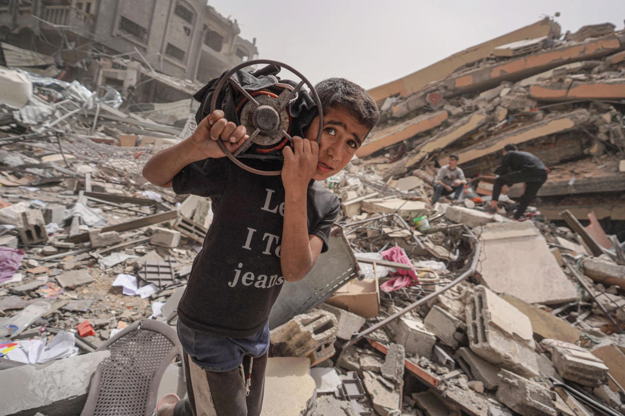 A Palestinian boy carries a gas cooker as he walks around the debris of a destroyed building in the city of Nuseirat in the central Gaza Strip on April 18, 2024, amid ongoing battles between Israel and the militant Hamas group. / Credit: AFP via Getty Images