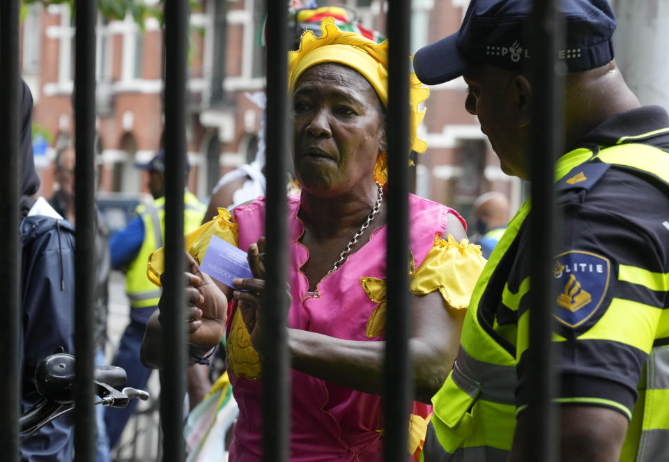 A woman mimics chains as she argues with a police officer to attend a nationally televised annual ceremony, closed for coronavirus related measures, in Amsterdam, Netherlands, Thursday, July 1, 2021. The ceremony and and celebration known as Keti Koti, which means Chains Broken, marks the abolition of slavery in its colonies in Suriname and the Dutch Antilles on July 1, 1863. Debate about Amsterdam's involvement in the slave trade has been going on for years and gained attention last year amid the global reckoning with racial injustice that followed the death of George Floyd in Minneapolis last year. (AP Photo/Peter Dejong)