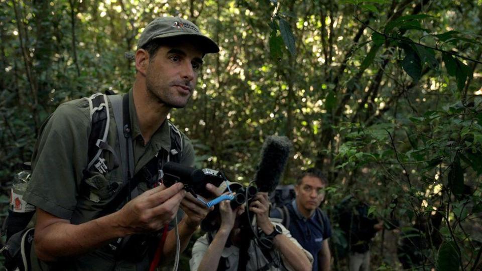 man in khaki shirt holds recording equipment in the forest