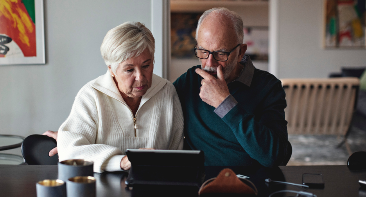 elderly couple sitting at table looking at black tablet, facebook portal