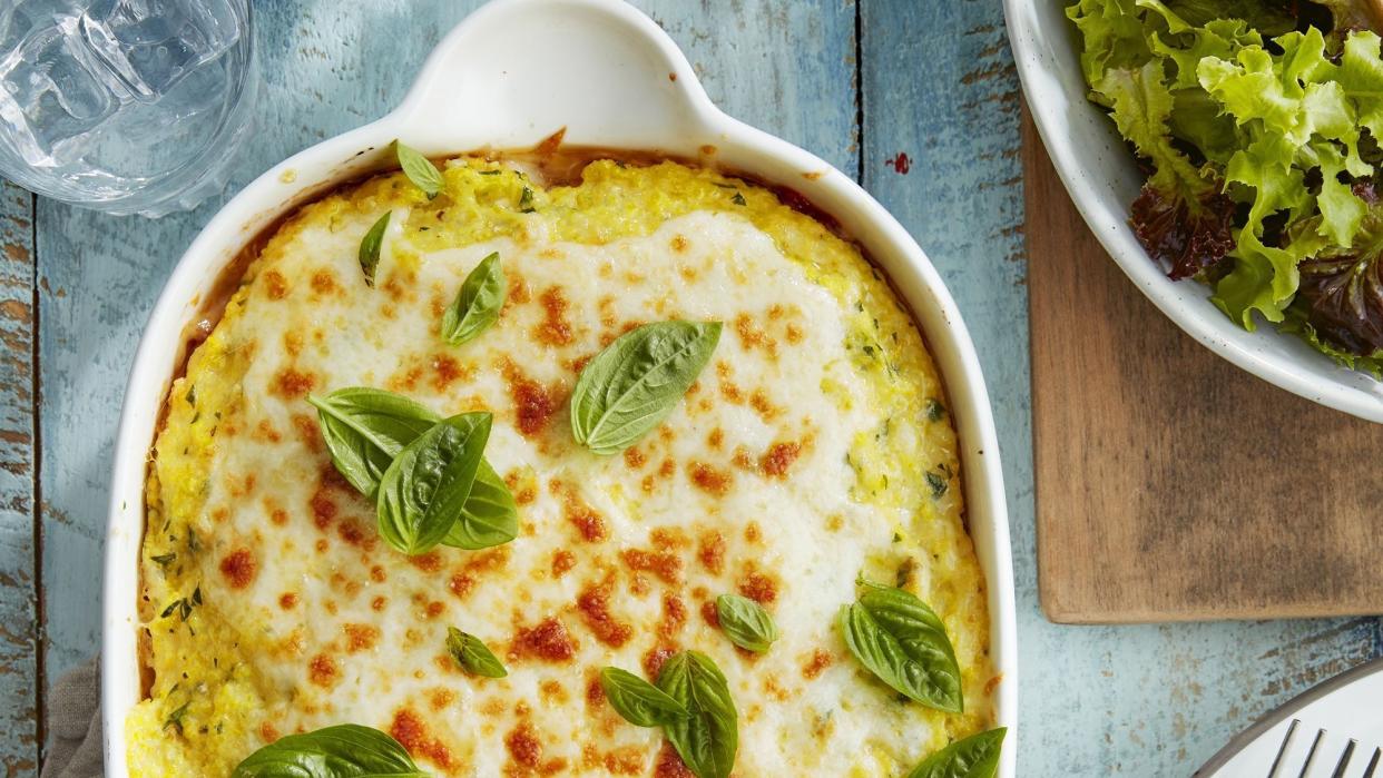 sausage grits lasagna in a white baking dish with fresh basil leaves on top