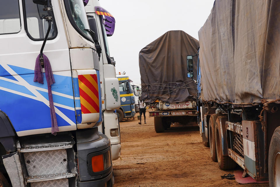 A driver walks between trucks in Niamey, Niger, Monday, Aug. 21, 2023. Around 300 trucks of food and other materials crossed into Niger from Burkina Faso with many arriving in the capital, Niamey Sunday, according to a regional custom's official. (AP Photo/Sam Mednick)