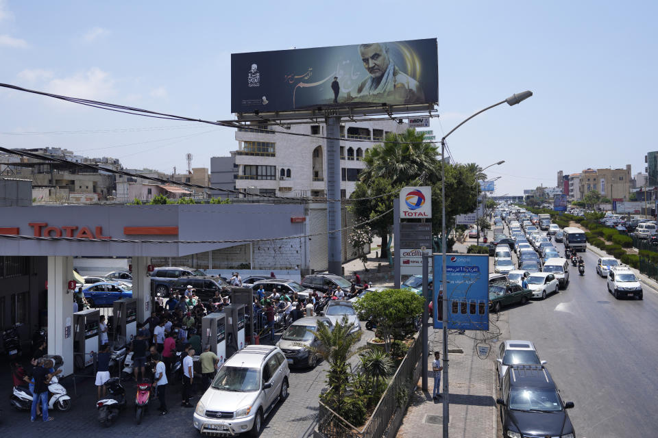 FILE - In this Sunday, June 27, 2021 file photo, drivers wait in a long line to get fuel at a gas station under a billboard showing Iranian Revolutionary Guard Gen. Qassem Soleimani, who was killed in Iraq in a U.S. drone attack in early January 2020, along the airport highway, in the southern suburbs of Beirut, Lebanon. Lebanon is struggling amid a 20-month-old economic and financial crisis that has led to shortages of fuel and basic goods like baby formula, medicine and spare parts. (AP Photo/Hassan Ammar, File)