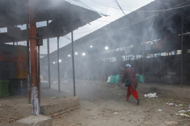 Woman runs away as disinfectant is sprayed from a vehicle inside a vegetable market during the lockdown in Kathmandu