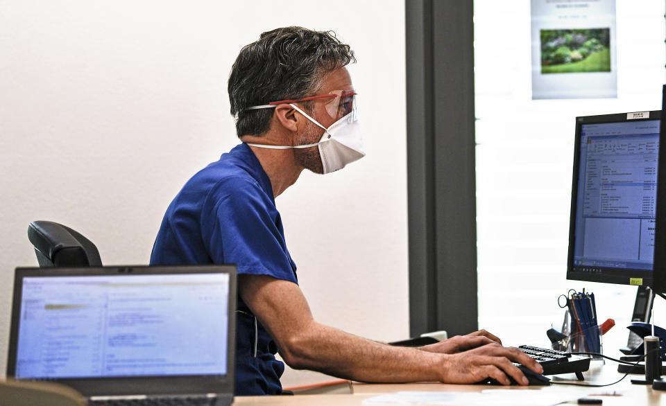 A doctor with a face mask to protect from coronavirus works in his office on a computer during a presentation for media of new emergency rooms at the University Hospital in Essen, Germany, Thursday, March 26, 2020. Hospitals in Germany ready themselves for an expected growing number of COVID-19 patients in the coming weeks. The new coronavirus causes mild or moderate symptoms for most people, but for some, especially older adults and people with existing health problems, it can cause more severe illness or death. (AP Photo/Martin Meissner)