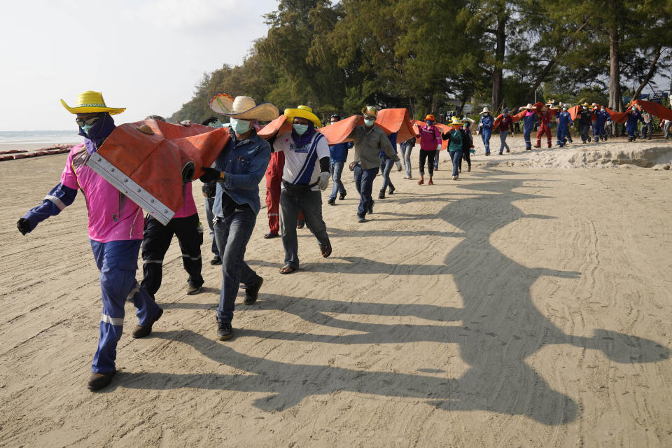 Workers carry an oil spill boom out onto Mae Ram Phueng Beach in hopes of containing any oil washing ashore from a recent spill off the coast of Rayong, eastern Thailand, Friday, Jan. 28, 2022. An oil slick off the coast of Thailand continued to expand Friday and was approaching beaches on the east coast, home to fragile coral and seagrass, officials said. (AP Photo/Sakchai Lalit)