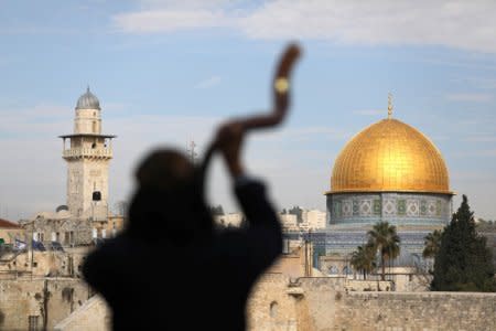 A man is silhouetted while he blows a Shofar, a ram horn, as the Dome of the Rock (R), located in Jerusalem's Old City on the compound known to Muslims as Noble Sanctuary and to Jews as Temple Mount, is seen in the background December 10, 2017. REUTERS/Ammar Awad