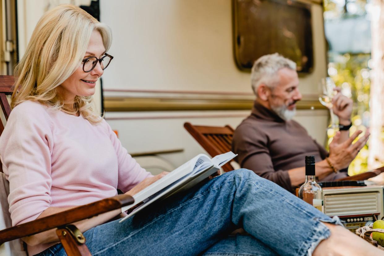 Close up portrait of mature blonde woman wearing glasses while reading near her husband and their trailer