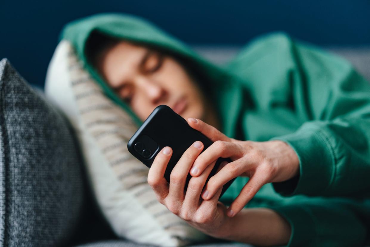 Teen boy wearing green hoodie on couch looking at phone.