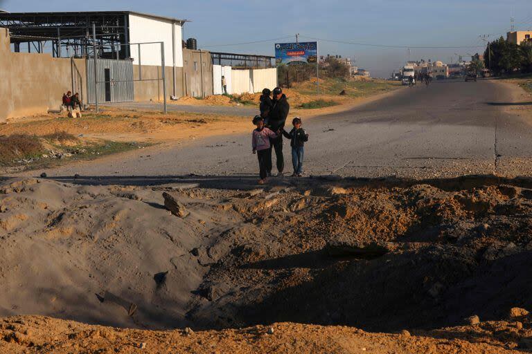 Los palestinos que huyen de Khan Yunis, en el sur de la Franja de Gaza, más al sur, hacia Rafah, contemplan un cráter causado por los bombardeos israelíes en la carretera de Salah Al-Din, el 10 de diciembre de 2023.