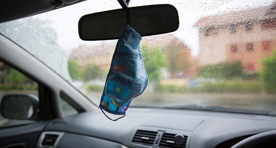 A face mask hangs from the rearview mirror of a car.