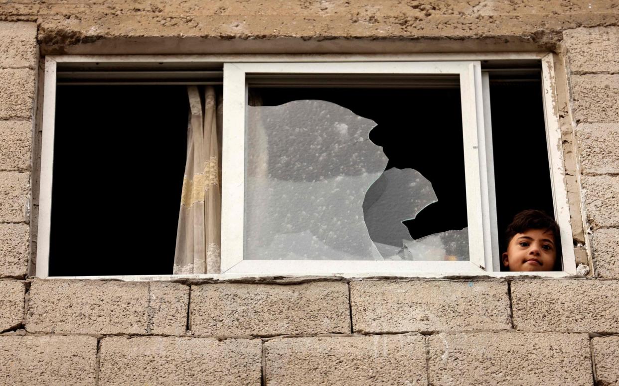 A Palestinian boy looks out of a damaged window following an Israeli airstrike at al-Shati Refugee Camp in Gaza City - AFP