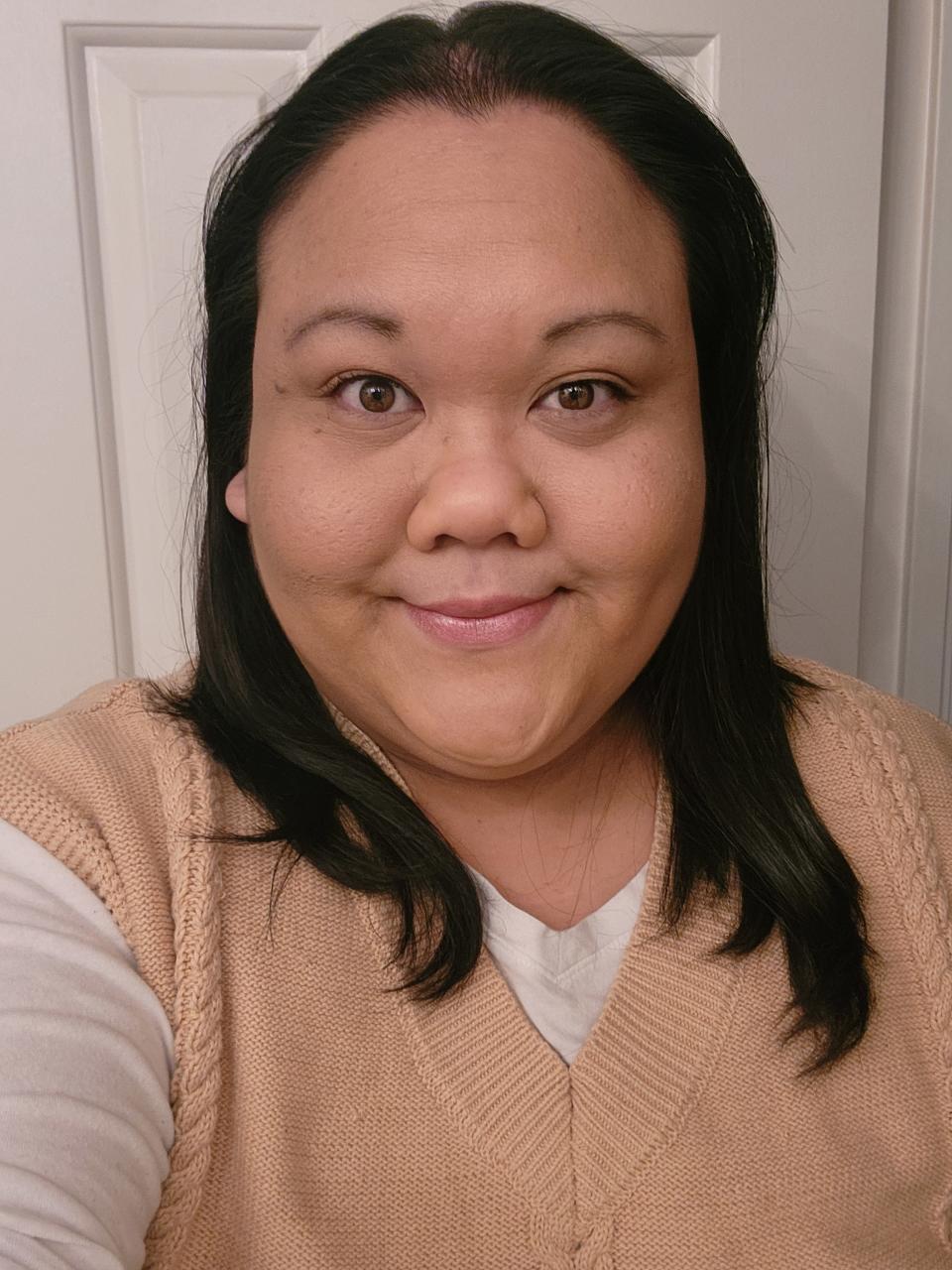 Brunette woman smiling with makeup wearing brown sweater