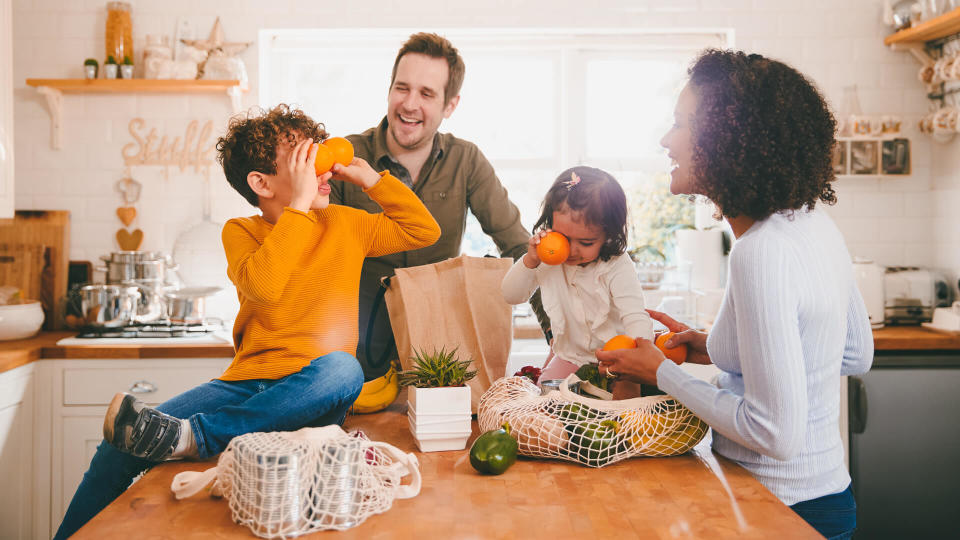 Family Returning Home From Shopping Trip Using Plastic Free Bags Unpacking Groceries In Kitchen.