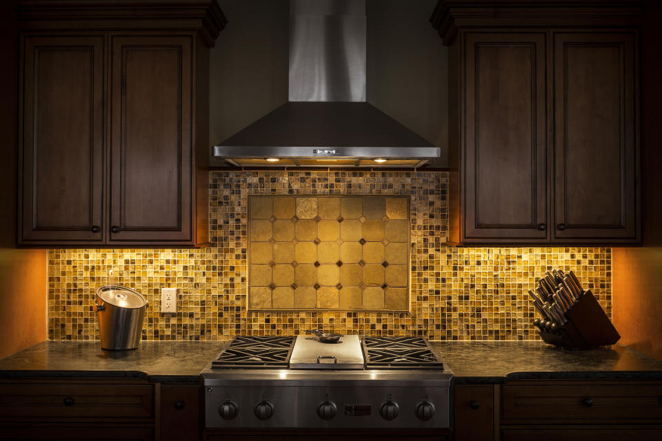 A modern kitchen with stainless steel stove, tiled backsplash, and wooden cabinets