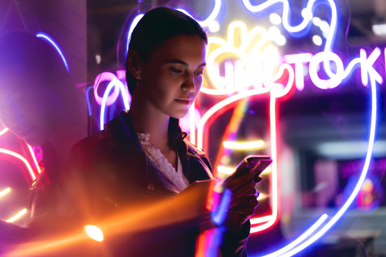 Progressive woman is using mobile phone at night in neon lights. Innovation, metaverse and futuristic concepts