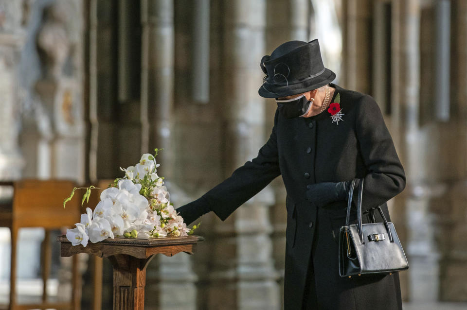 Britain's Queen Elizabeth II inspects a bouquet of flowers to be placed at the grave of the Unknown Warrior by her Equerry, Lieutenant Colonel Nana Kofi Twumasi-Ankrah, in Westminster Abbey, London, Wednesday, Nov. 4, 2020. Queen Elizabeth II donned a face mask in public for the first time during the coronavirus pandemic when attending a brief ceremony at Westminster Abbey last week to mark the centenary of the burial of the Unknown Warrior. While the 94-year-old has been seen in public on several occasions over the past few months, she has not worn a face covering. (Aaron Chown/Pool Photo via AP)